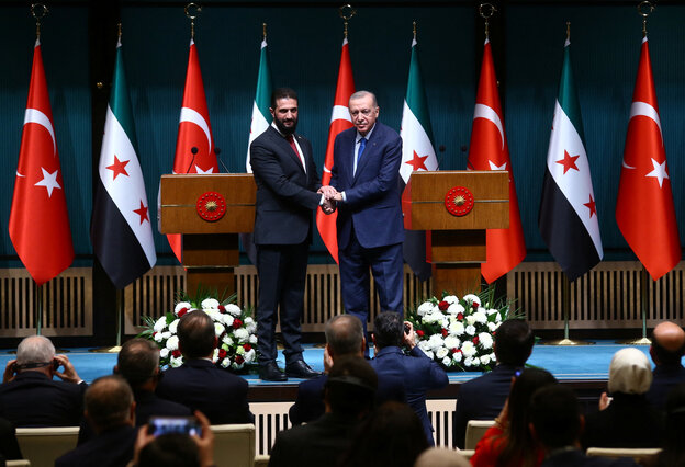 Zwei Männer schütteln sich vor den Fahnen Syriens und der Türkei die Hand . Links steht Scharaa, rechts der sehr viel ältere Erdoğan.