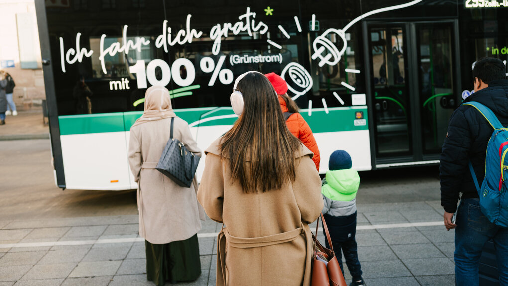 Mehrere Frauen warten an einer Haltestelle, ein Bus fährt ein mit der Aufschrift "Ich fahr dich gratis"