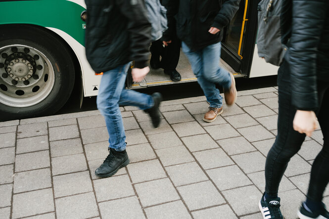 3 Menschen kommen aus einem Bus, wir sehen ihre Beine