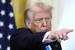 Trump zeigt mit dem Finger, im Hintergrund zwei Fahnen