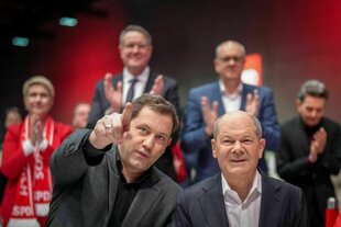 Lars Klingbeil sitzt neben Olaf Scholz und zeigt mit seinem Finger in eine Richtung