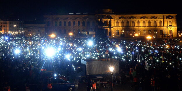 Pegida-Demonstranten halten im Dunkeln ihre leuchtenden Handys hoch