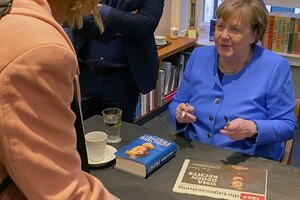 Silke Burmester und Angela Merkel, die lächelnd die taz signiert