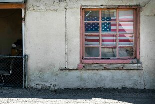 Fassade eines heruntergekommenen Hauses mit einer verblichenen, hinter einem vergitterten Fenster hängenden US-Flagge