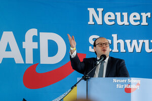 Krzysztof Walczak spricht auf einer Bühne vor einem AfD-Plakat