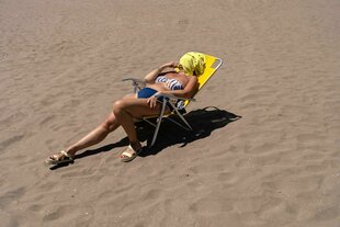 Eine Frau nimmt ein Sonnenbad am Strand, ihr Gesicht is mit einem gelben Handtuch bedeckt.