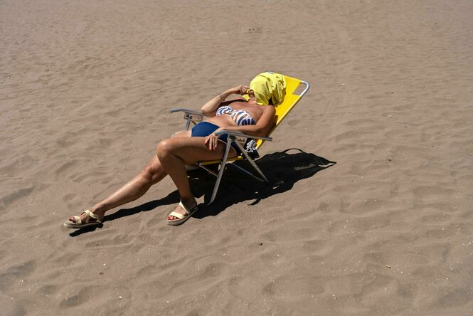 Eine Frau nimmt ein Sonnenbad am Strand, ihr Gesicht is mit einem gelben Handtuch bedeckt.