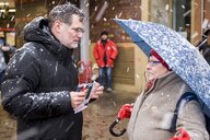 Wolfgang Schmidt steht im Schneefall einer Frau gegenüber, die sich mit einem regenschirm schützt