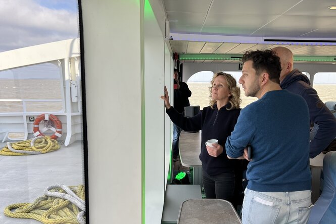 Eine Gruppe Menschen schaut besorgt aus dem Fenster eines Schiffes