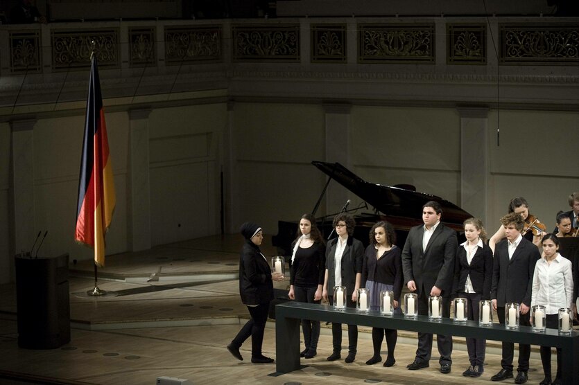 Die Angehörigen der Opfer des NSU stehen in einem Kirchenraum hinter weißen Kerzen, am Rand des Raumes eine Fahne der Bundesrepublik Deutschland