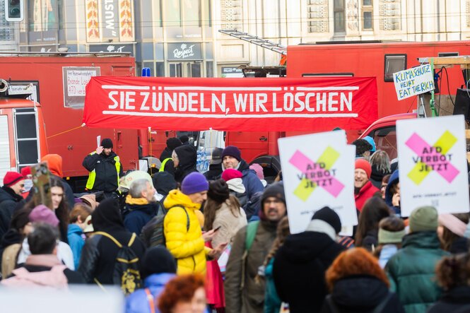 Eine Menschenmenge auf der Straße und große Feuerwehrautos im Hintergrund