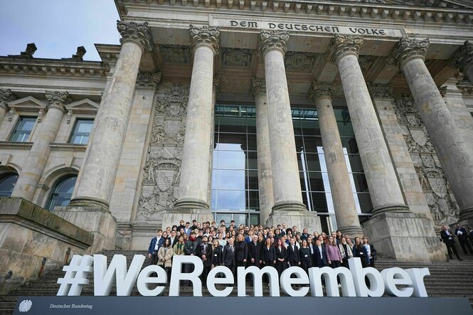 Die Teilnehmer einer Gedenkstunde stehen auf den Stufen des Reichstages hinter dem Schriftzug "#We Remember".