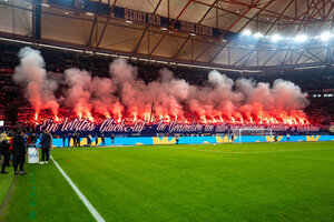 Zu sehen sind Schalke-Fans im Stadion mit Bengalo-Fackeln in einer Choreo.