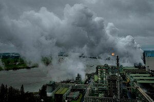 Thyssenkrupp-Stahlwerk in Duisburg. Aus einem Schlot dringt Qualm oder Rauch. Alles ist grau und düster. Im Hintergrund: Eine Waldgrenze, die größtenteils vom Rauch verdeckt wird.