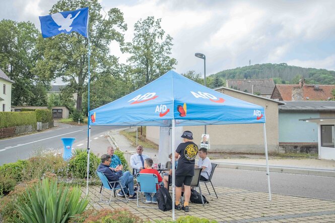 AFD Zeltstand an einer ländlichen Straßenkreuzung, junge Menschen hocken auf Stühlen