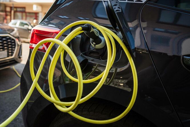 Ein gelbes Ladekabel steckt in einem Schwarzen E-Auto