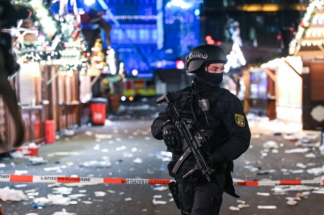 Ein Maschinengewehr bewaffner Polizist läuft über einen abgesperrten Weihnachtsmarkt