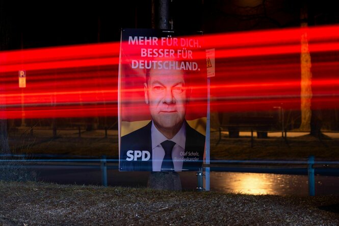 Rot verschwommener Streifen durch eine Langzeitaufnahme läuft über ein Plakat des Olaf Scholz