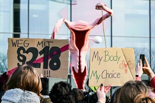 Demonstrierende mit einem überdimensionalen Uterus für sexuelle Selbstbestimmung welcher die Hand erhebt und Schildern für Schwangerschaftsabbrüchen