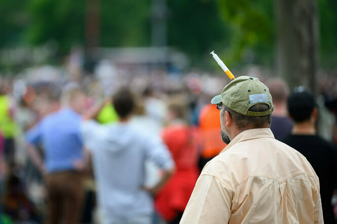 Person mit einer Spritze an seiner Basecap vor eioner Demonstration