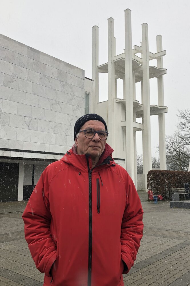 Älterer Mann in roter Jacke steht im Schnee