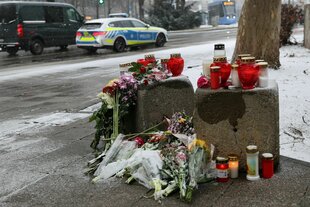 Blumen und Kerzen sind an der Stelle zu sehen, wo am Donnerstag ein Auto in in eine Verdi-Demonstration gerast war. Im Hintergrund fährt ein Polizeiauto vorbei.