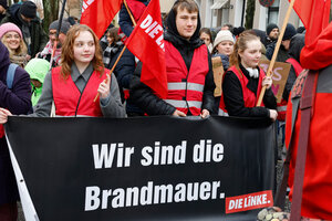 Ein schwarzes Transparent, junge Menschen in roten Westen