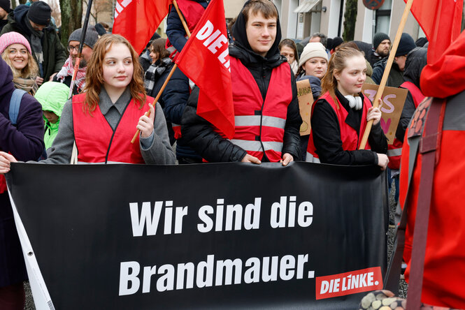 Ein schwarzes Transparent, junge Menschen in roten Westen