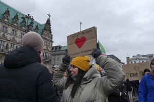 eine Frau hält ein Pappschild mit einen roten Herzen und der Aufschrift 