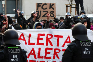 Polizisten stehen vor einem Banner auf dem "Alerta, Alerta" steht