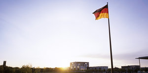 Deutschland-Flagge mit Teilen des Kanzleramts im Hintergrund.