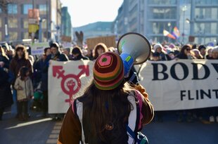 Eine Frau von hinter mit Megafon auf einer Demonstration