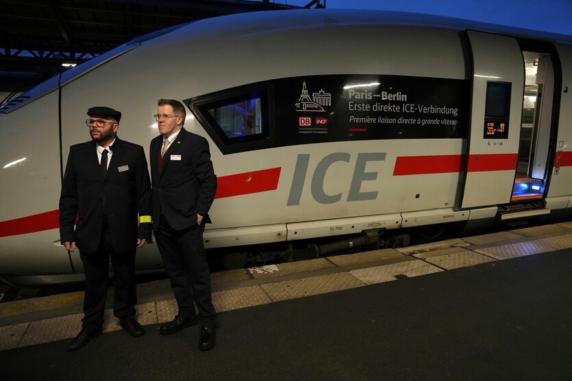 Zwei Mitarbeiter der Deutschen Bahn neben einem stehenden ICE. Auf dem Zug steht „Paris-Berlin. Erste ICE-Direktverbindung“