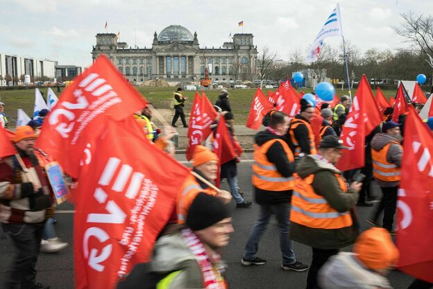 Beschäftigte der Bahn demonstrieren in Warnwesten und mit roten EVG-Flaggen auf einer Straße vor dem Reichstagsgebäude