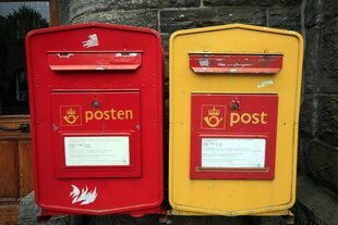 Zwei Briefkästen in den Farben rot und gelb - sind an einer Wand befestigt