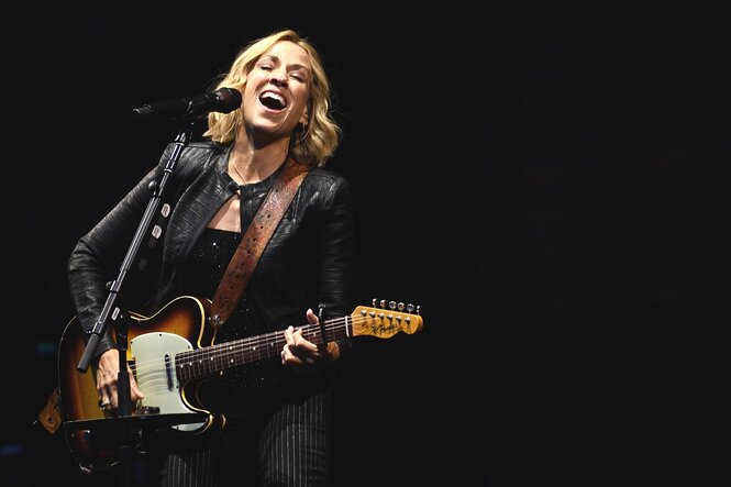 Sheryl Crow mit Gitarre, sie singt in ein Mikrofon