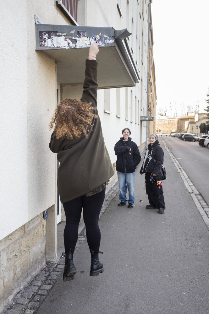 Eine junge Frau springt in die Luft, um Aufkleber an einer Hausfassade zu entfernen