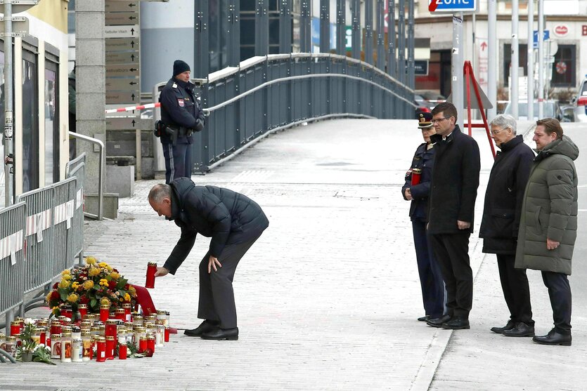 Politiker am Tatort - einer stellt eine rote Trauerkerze zu den Blumen und Kerzen, vier andere stehen in gebührendem Abstand hinter ihm