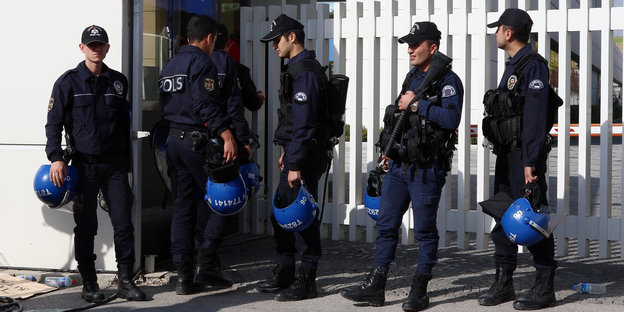 Fünf türkische Polizisten in schwerer Uniform stehen vor einem weißen Zaun