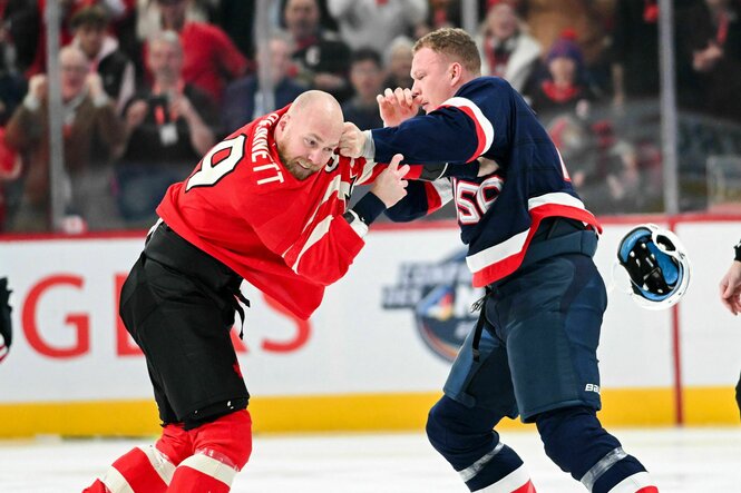 Zwei Eishockeyspieler schlagen sich, ein Helm fliegt vom Kopf