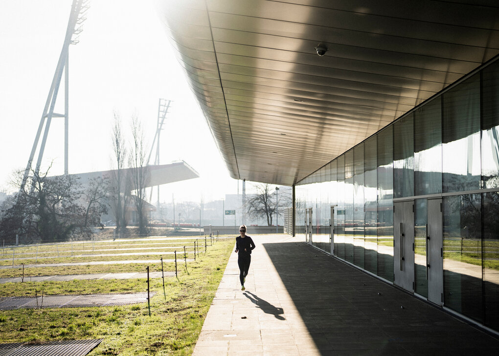 Eine Person in Laufausrüstung läuft alleine in einem Sportpark in Berlin