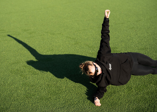 Eine Person ist aufgestützt auf einem Arm und den Füßen im Gras, sie macht einen Sideplank. Der andere Arm ist in die Luft gestreckt.