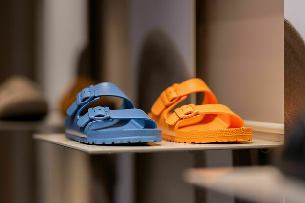 Zwei Birkenstocksandalenin den Farben blau und orange stehen in einem Schaufenster