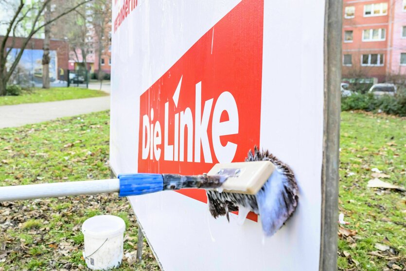 Ein Wahlplakat auf dem "Die Linke" steht, wird mit einem Besen voller Kleister angebracht