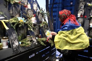 Eine Frau, die in eine ukrainische Flagge gehüllt ist, stellt Blumen und eine Kerze vor das Foto eines Gefallenen auf