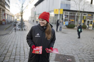 Maja Wallstein steht mit SPD Wahlmaterial, in schwarzer Adidas Jacke und roter Mütze in einer Fußgänger:innen Zone und lächelt