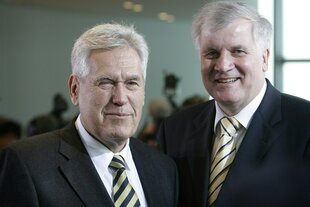 Michael Glos schaut mit einem verkniffenen Blick und einem Auge zu in die Kamera, neben ihm Horst Seehofer