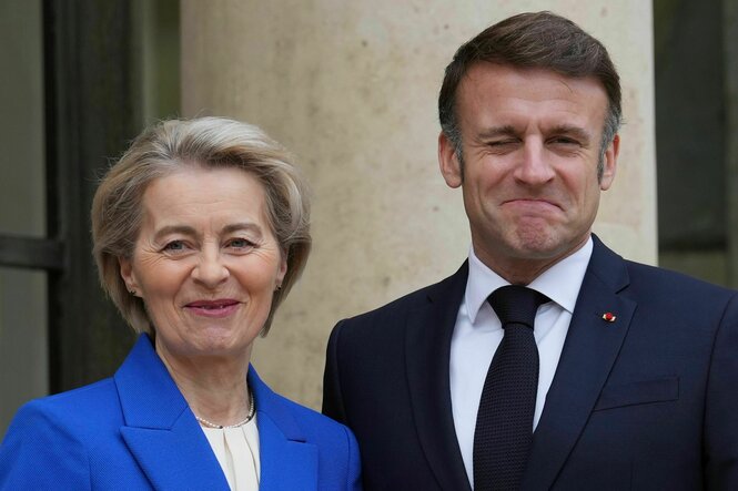 Von der Leyen schaut normal in die Kamera, Macron blinzelt leicht ironisch