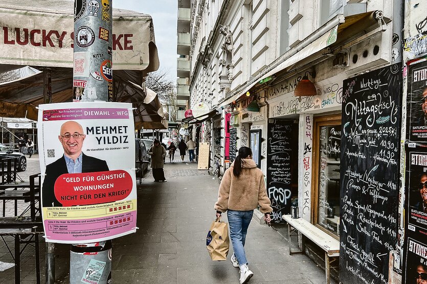 Mann auf einem Plakat an einem Laternenpfahl neben Altbaufassaden