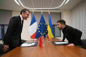 Emmanuel Macron und Wolodymyr Selenskyj nehmen vor einem Treffen an einem Tisch ihre Plätze ein, im Hintergrund ist die französische, die EU und die ukrainische Flagge